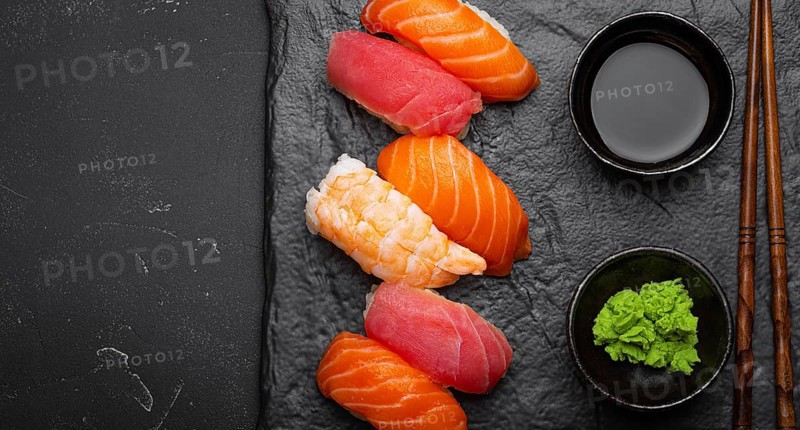 Traditional Japanese sushi with soy sauce, wasabi, chopsticks top view on dark black rustic slate. Sushi with salmon, tuna and shrimp, space for text, food photography, food photography