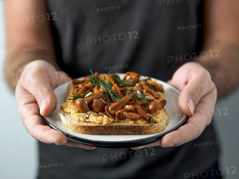 Hands takes plate with vegan sandwich. Healthy appetiezer - whole wheat bread toast with chickpea hummus and honey fungus mushrooms