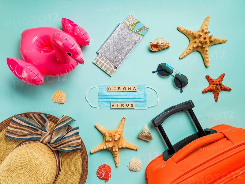 Coronavirus covid-19 and travel concept. Summer vacation and beach rest symbols and breathing mask with wood letters coronavirus on blue background. Flat lay or top view