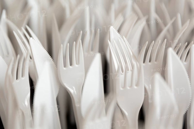 White plastic forks and knifes are seen stacked. Most disposable plastic utensils are made of polystyrene