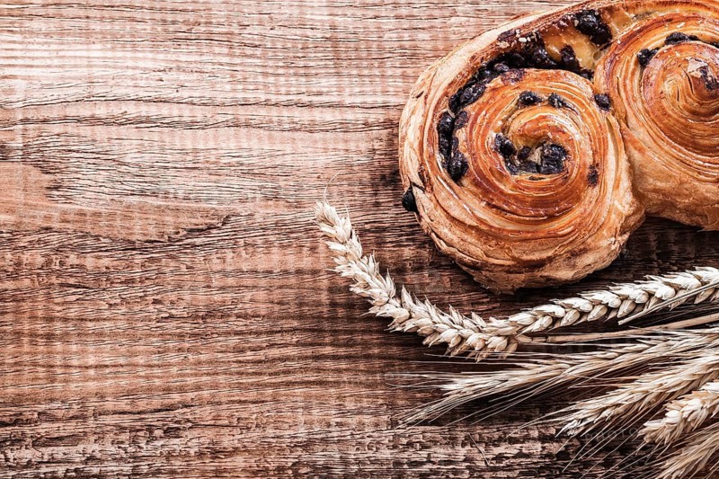 Roll with raisins wheat ears on oak wooden board food and drink concept
