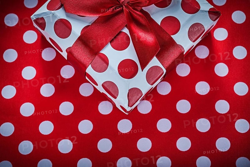 Present box with tied ribbon on polka-dot red tablecloth celebrations concept
