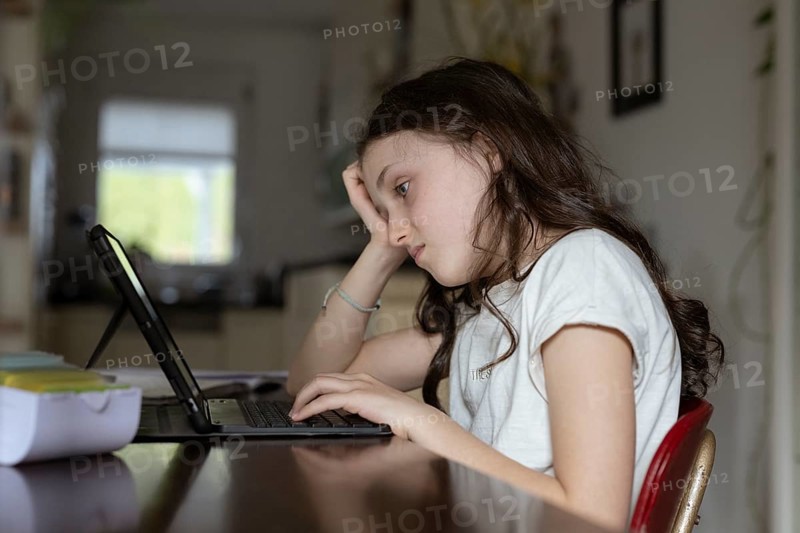 Girl, 10 years old, sits at the table with a tablet and learns