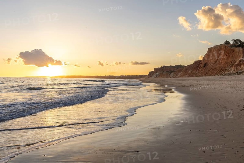 The golden sandy beach of Praia da Falésia, crystal clear sea water at low tide with the reflection of the sky, the setting sun and the characteristic orange-coloured cliffs, Algarve, Portugal, Europe