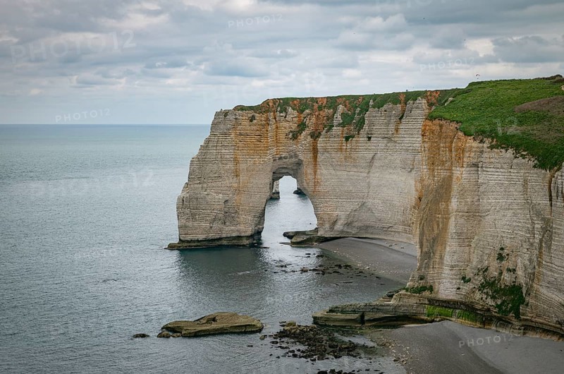 Landscape photo of tall, steep limestone cliffs by the ocean with one with a hole in it creating an arch