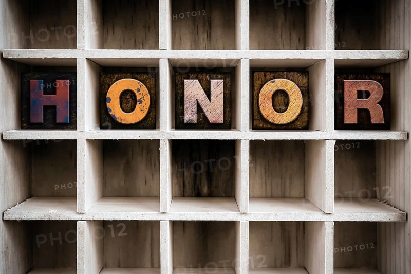 The word HONOR written in vintage ink stained wooden letterpress type in a partitioned printer's drawer