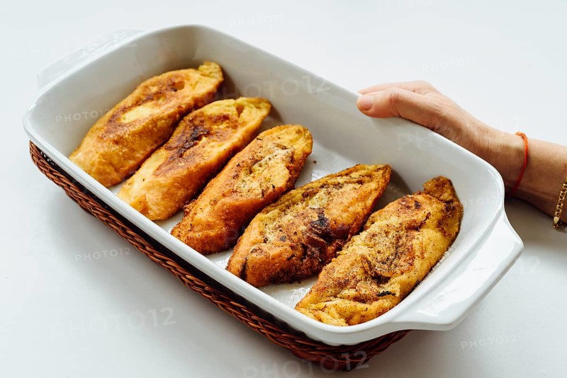 Female hand holding a tray with torrijas, a typical Spanish sweet fried toasts of sliced bread soaked in eggs and milk, on white background. Traditional dessert for Lent and Easter