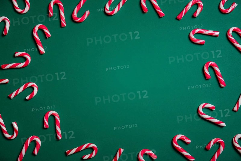 Christmas sweets frame with mini candy canes in red and white stripes, on a green paper background with empty space in the middle