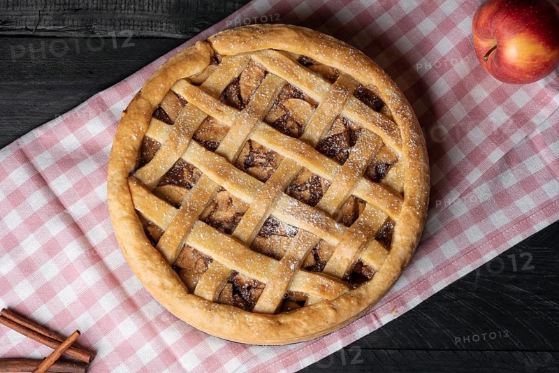 Above view of a delicious homemade apple pie with a lattice crust, on a pink towel, on a wooden table. Freshly baked desserts. National pie day