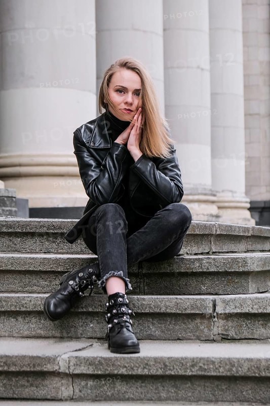 Portrait of young blonde woman with red lips wearing leather jacket on corporate building stairs. Career businesswoman. Stylish female biker. Urban street city lifestyle