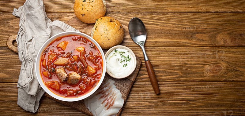 Ukrainian Borscht, red beetroot soup with meat, in white bowl with sour cream, garlic buns Pampushka and salo slices on rustic stone background. Traditional authentic dish of Ukraine, space for text, food photography, food photography