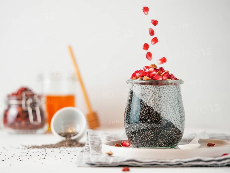 Healthy breakfast concept and idea - two colors chia pudding with organic raw pomegranate. Glass jar with black charcoal and white vegan milk chia pudding with falling pomegranate. Copy space