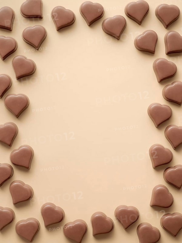 Frame of romantic chocolate confections in heart shapes on pastel yellow background. Canvas with heart chocolate sweets on champagne beige background. Copy space. Valentines day background. Vertical