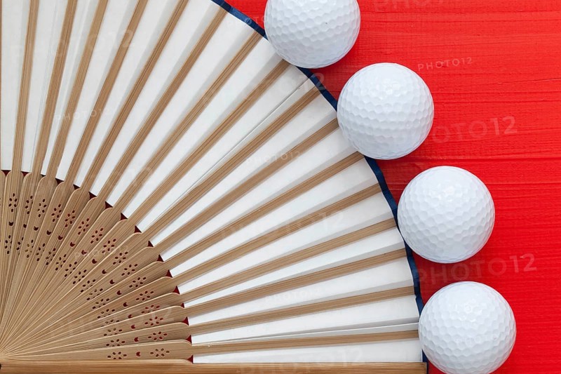 Typical Japanese hand fan made and golf balls on the wooden red table