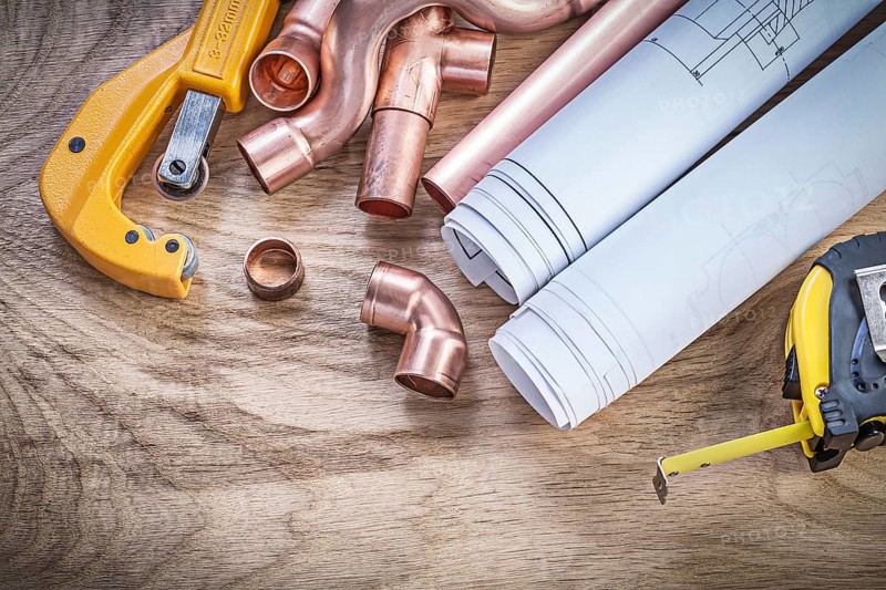 Construction drawings measuring tape copper water pipe cutter fittings on wooden board plumbing concept