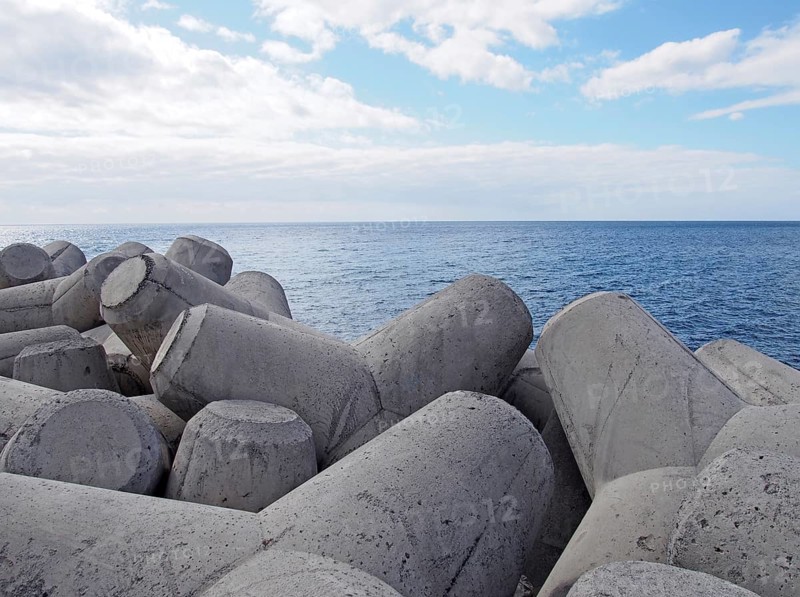 Concrete interlocking tetrapods used to prevent coastal erosion placed on a shoreline with a blue sea and sunny sky