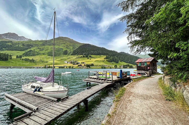 Sailing boat at a jetty on a lake, surrounded by mountains and green nature, under a cloudy sky, Davos, Switzerland, Europe