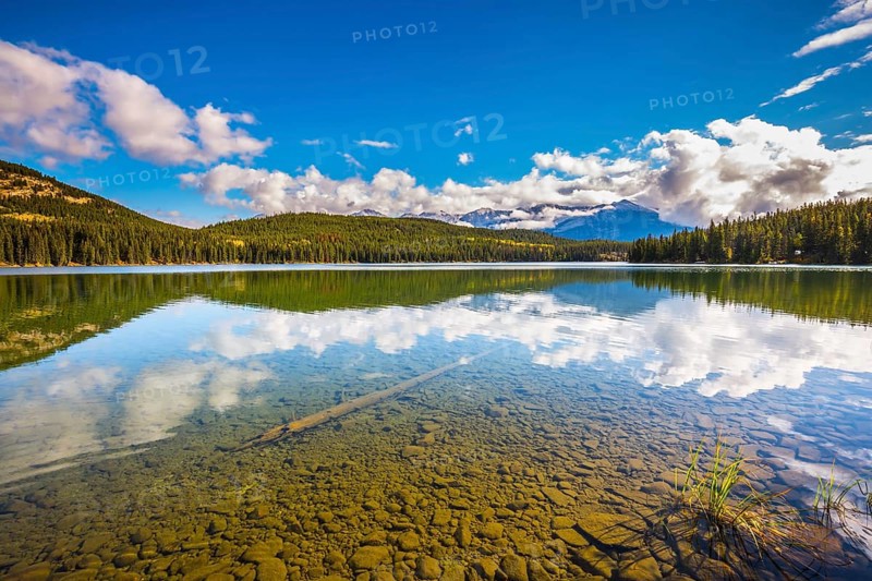 Clear water Pyramid Lake reflects the clouds and pine forests on shore. Frosty morning in the Rocky Mountains, Canada, North America