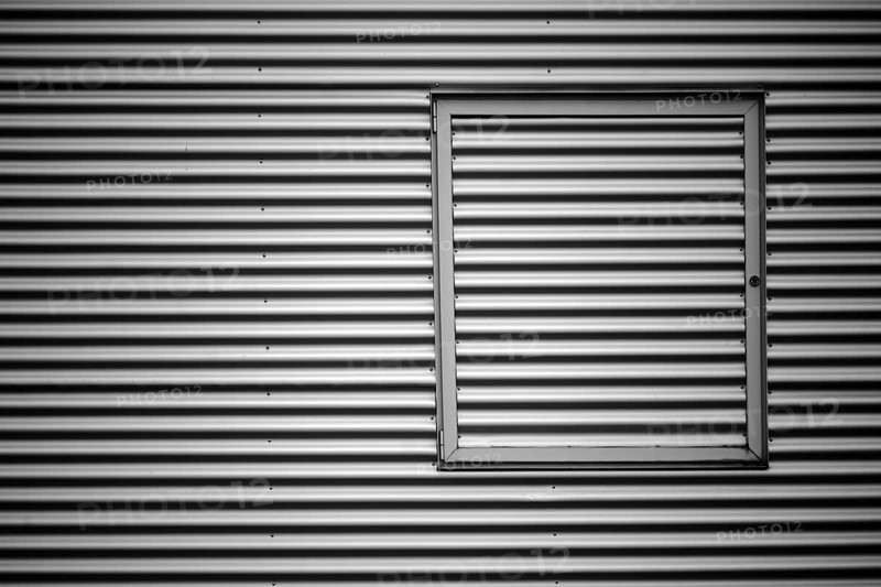 Close-up of the corrugated sheet metal façade of an industrial building with a metal window frame
