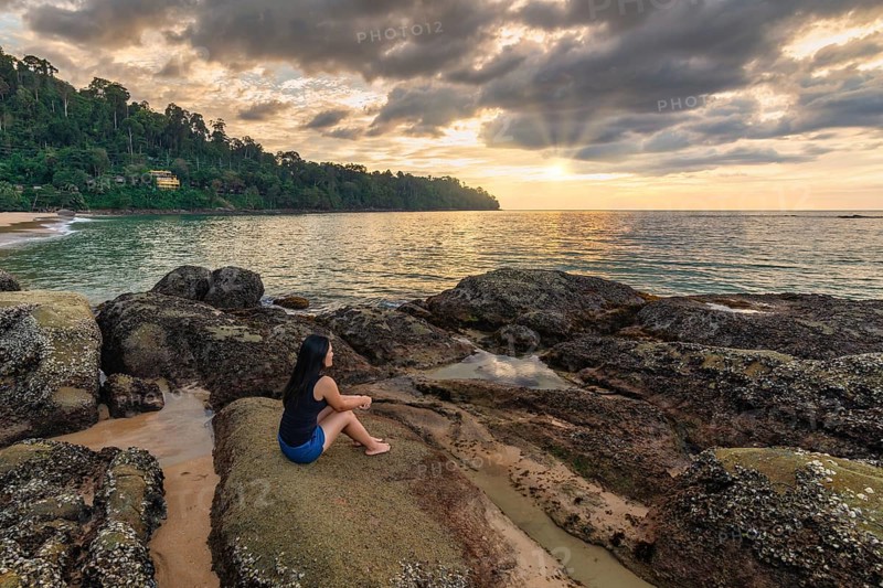 Tropical sea beach sunset with woman tourist on rock coast and ocean wave at Khao Lak, Phang Nga Thailand nature landscape