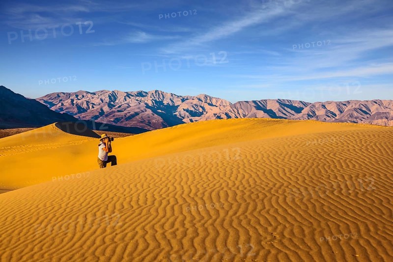Woman in striped shirt and straw hat photographing sand waves. Bright morning in picturesque part of Death Valley. Mesquite Flat Sand Dunes