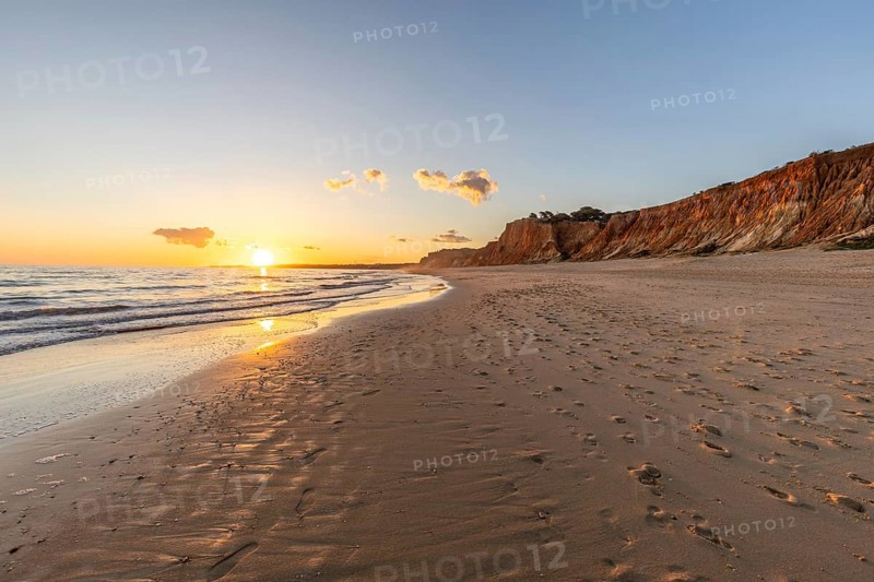 Beautiful sandy beach with red rocks and cliffs. Twilight at sunset with shallow waves on the Atlantic coast in Praia do Poço Velho, Praia da Falésia, Algarve, Portugal, Europe