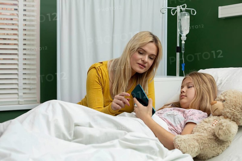 In a heartfelt hospital moment, a woman and a girl share a phone, reinforcing their connection in a challenging time