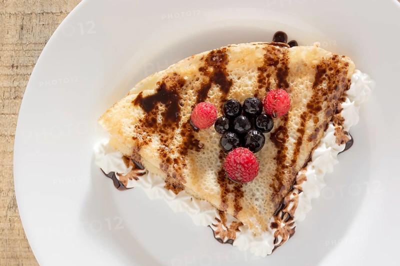 Fresh, golden pancakes with fruit and cream on a white plate with blurred background