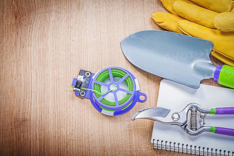 Protective gloves pruning shears garden tie wire hand shovel notepad on wooden board gardening concept