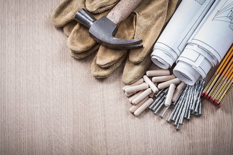 Wooden meter dowels blueprint rolls claw hammer leather protective gloves and metal nails on wood board construction concept