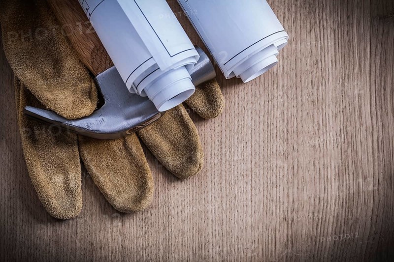 Construction drawings protective gloves and claw hammer on wooden board