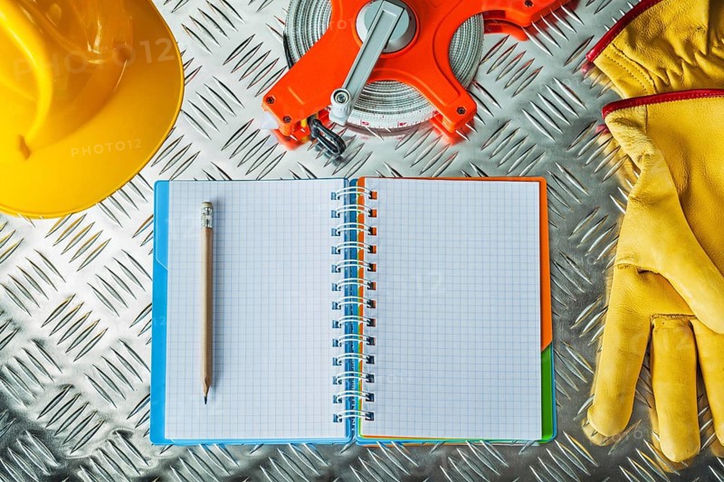 Safety gloves hard hat tape measure notebook pencil on corrugated metal sheet