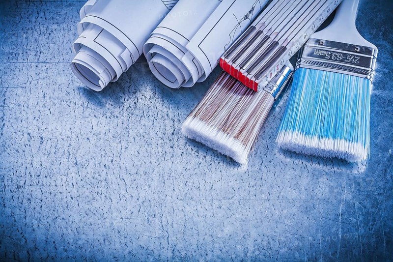 Paintbrushes wooden meter blueprints on metallic background close up view