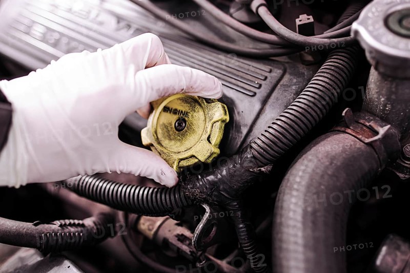 A gloved hand removing the cap from a car engine for maintenance
