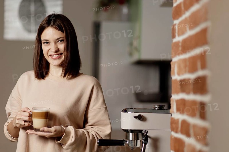 Woman with a cup of coffee beside an espresso machine and brick wall