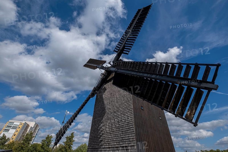 Germany, Berlin, 19.09.2023, Marzahner Bockwindmühle, a trestle windmill in Berlin-Marzahn, the name of the mill type says it all: the mill house stands vertically on a single thick beam, the house tree, which ends just above the ground. The house beam is supported by a four-footed trestle. This allows the mill, which is more than 14 metres high, to be rotated through 360 degrees. Wooden bollards are placed around the mill. They mark the minimum distance so that nobody is hit by the rotating wind blades, which have a span of around 20 metres. 01, Europe