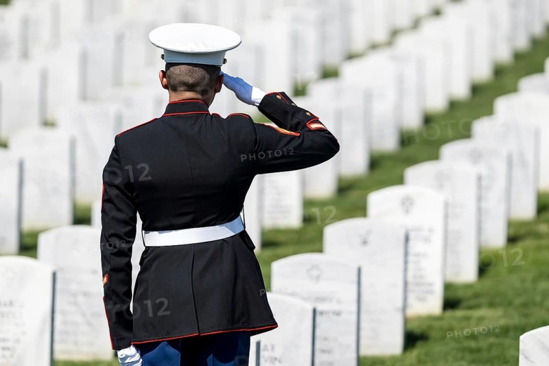 A poignant moment unfolds as a Marine plays taps, honoring a fallen veteran with a solemn salute, marking their internment at a national military cemetery