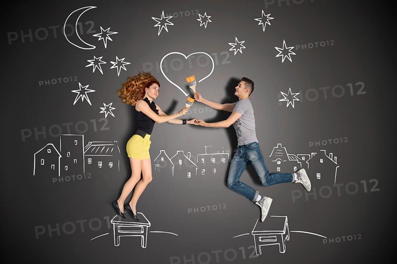 Happy valentines love story concept of a romantic couple standing on a stool and painting a heart in the night sky against chalk drawings background