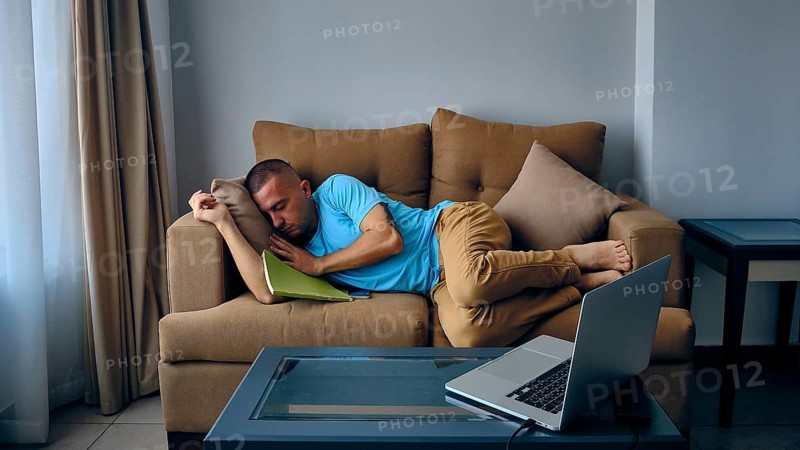 Young adult caucasian man felt asleep on a couch in front of laptoe. Tired man sleeps on sofa
