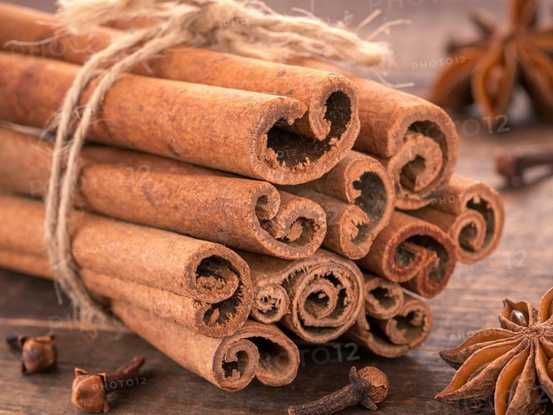 Ground cinnamon, cinnamon sticks, tied with jute rope on wooden background. Clove and star anise as background