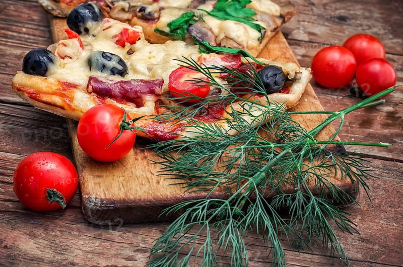 Hunk of delicious meat pizza with bacon and olives on the background of the vegetables.The image is tinted