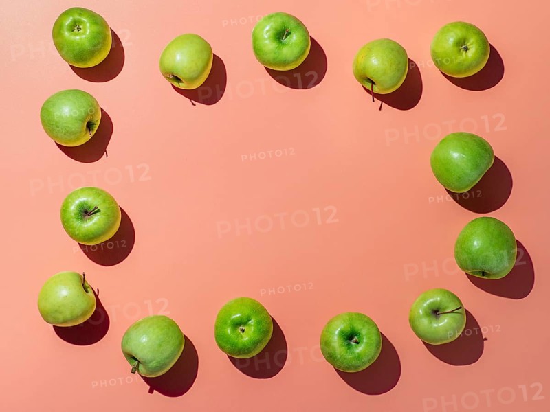 Green apples on orange or coral pink background with copy space for text or design in center, Colorful fruit frame. Flat lay or top view, Hard light