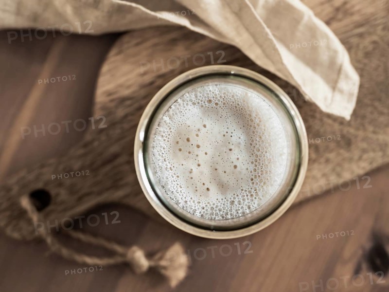 Wheat sourdough starter. Top view of glass jar with sourdough starter on wooden cutting board. Copy space for text or design