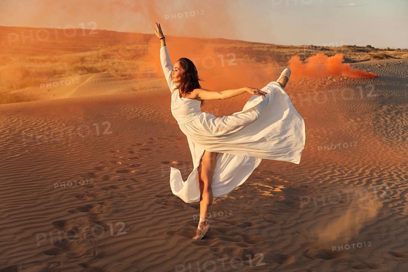 A girl in a fly white dress dances and poses in the sand desert at sunset