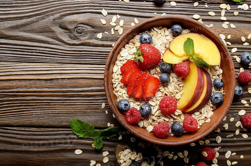 Flat lay of fruit healthy muesli with peaches strawberry almonds and blackberry in clay dish on wooden kitchen table