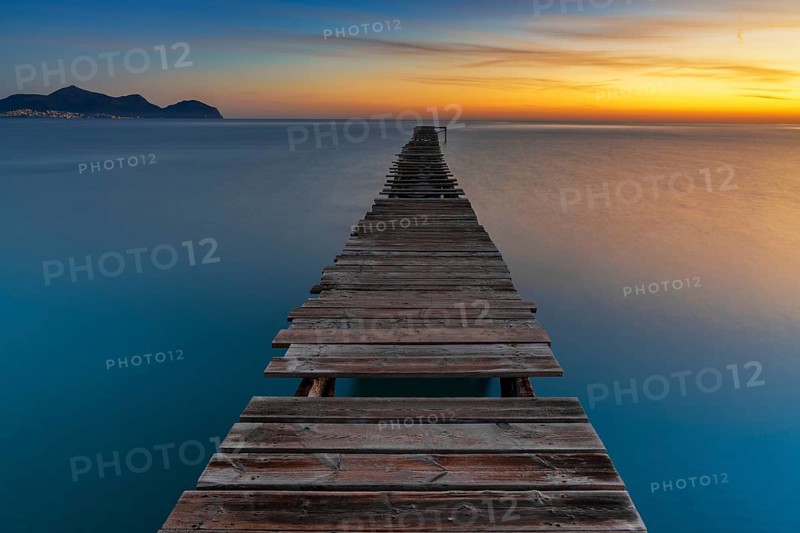 Peaceful sunrise seascape with an old wooden dock leading out into the calm ocean waters of Alcudia Bay
