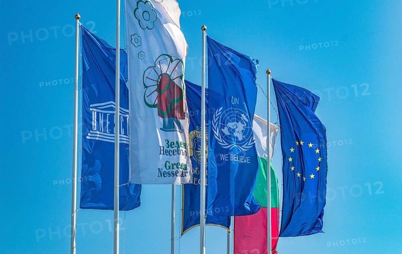 The Flags of European Union, United Nations, Unesco, Bulgaria, and Nessebar city waving in the wind. EU, UN, Unesco, Bulgaria, and Nessebar flags against a blue sky, Europe