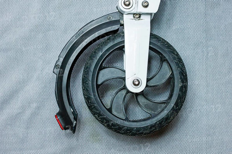 Front wheel and tire of a scooter with a black tire and metal attachment on a grey backdrop