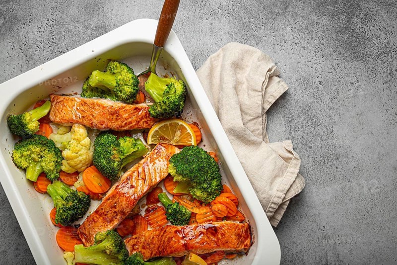 Top view of healthy baked fish salmon steaks, broccoli, cauliflower, carrot in casserole dish on gray stone background. Cooking a delicious low carb dinner, healthy nutrition concept. Space for text, food photography