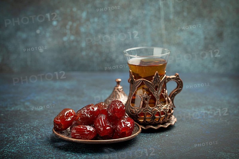 Breaking fasting with dried dates during Ramadan Kareem, Iftar meal with dates and Arab tea in traditional glass, angle view on rustic blue background. Muslim feast, food photography, food photography
